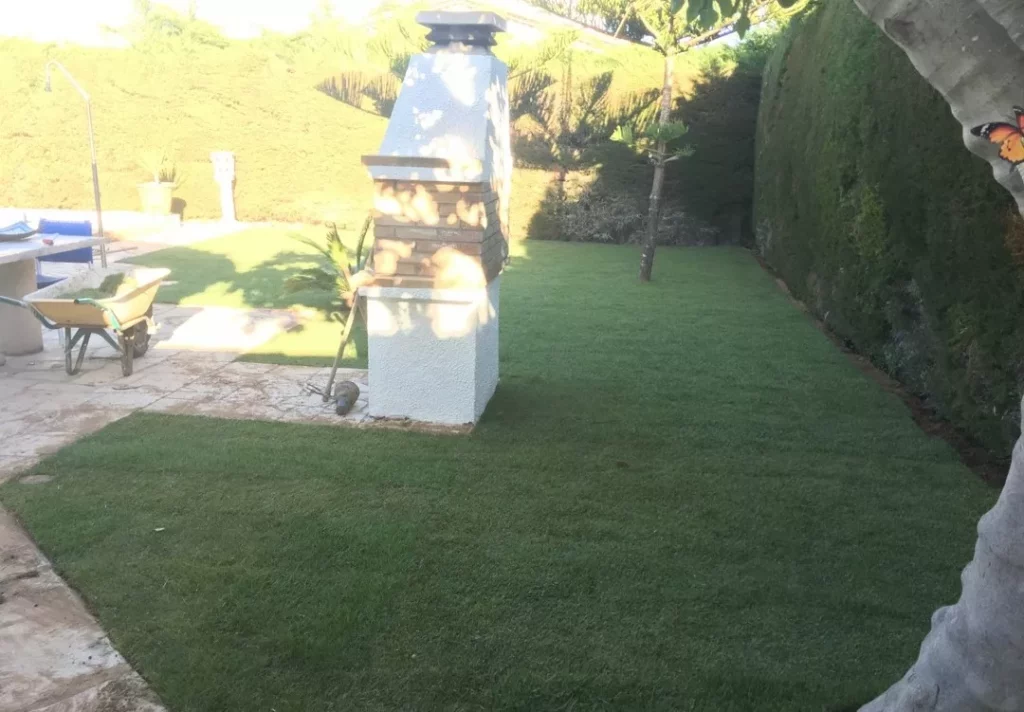 Césped verde y tupido rodeando una barbacoa de obra blanca