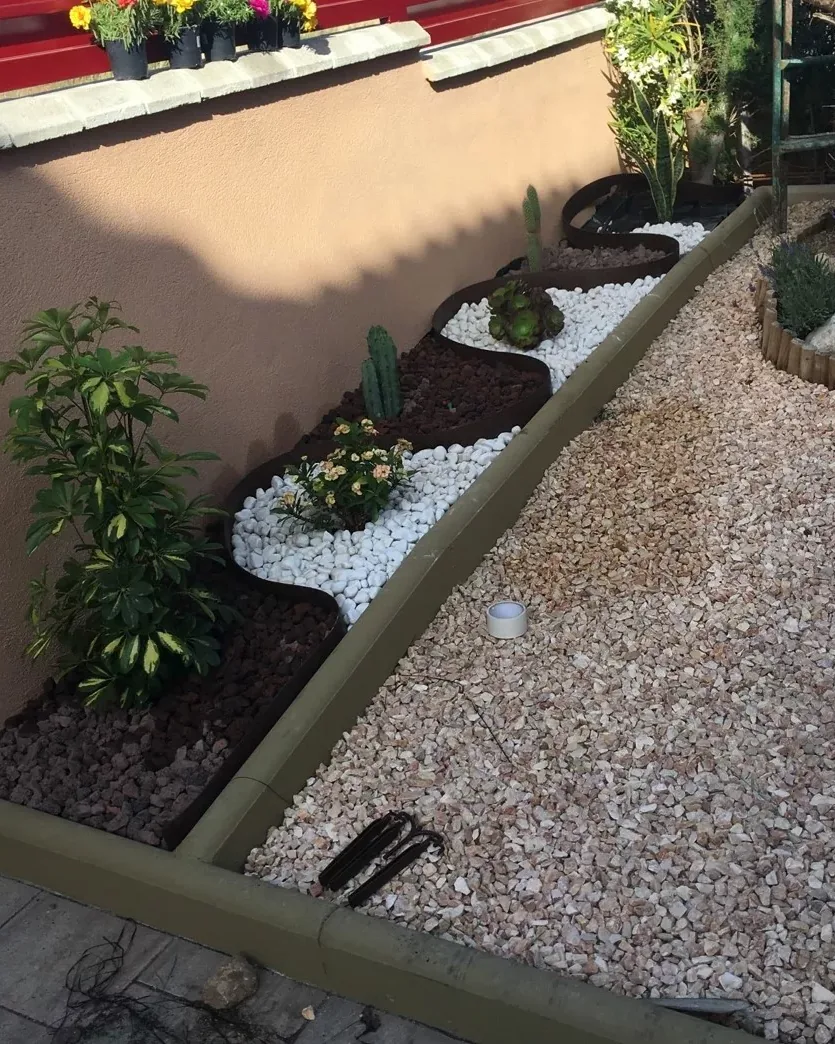Parterre decorado con grava blanca y marrón, plantas y cactus junto a una pared