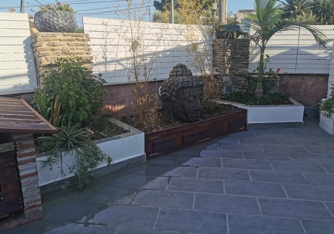 Jardineras elevadas de madera con plantas, esfera de piedra y pavimento de losa gris
