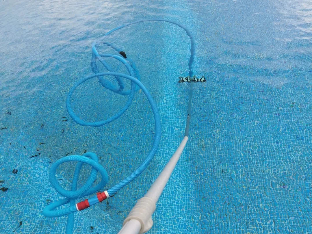 Limpiafondos manual con manguera flotante trabajando en el fondo de una piscina