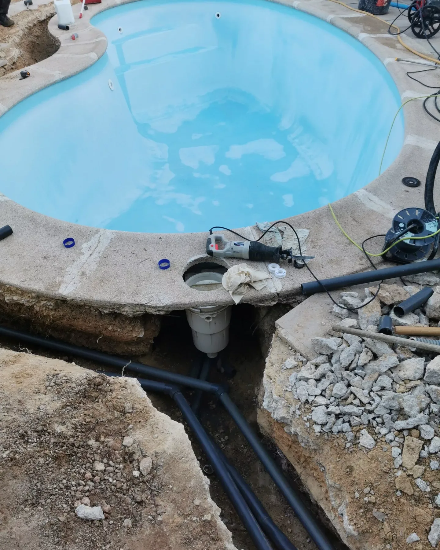 Piscina de forma curva en obra con zanja abierta y tuberías negras a la vista