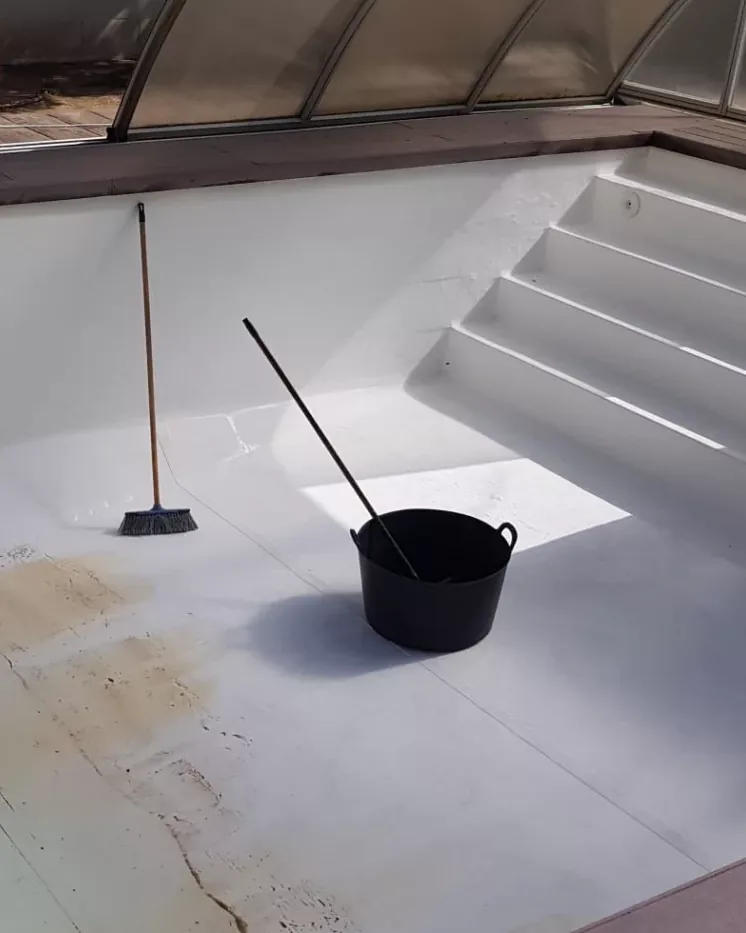 Interior de una piscina recién pintado de blanco con manguera y cubo de obra