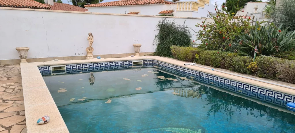 Piscina con cenefa de greca azul y agua verdosa antes del tratamiento