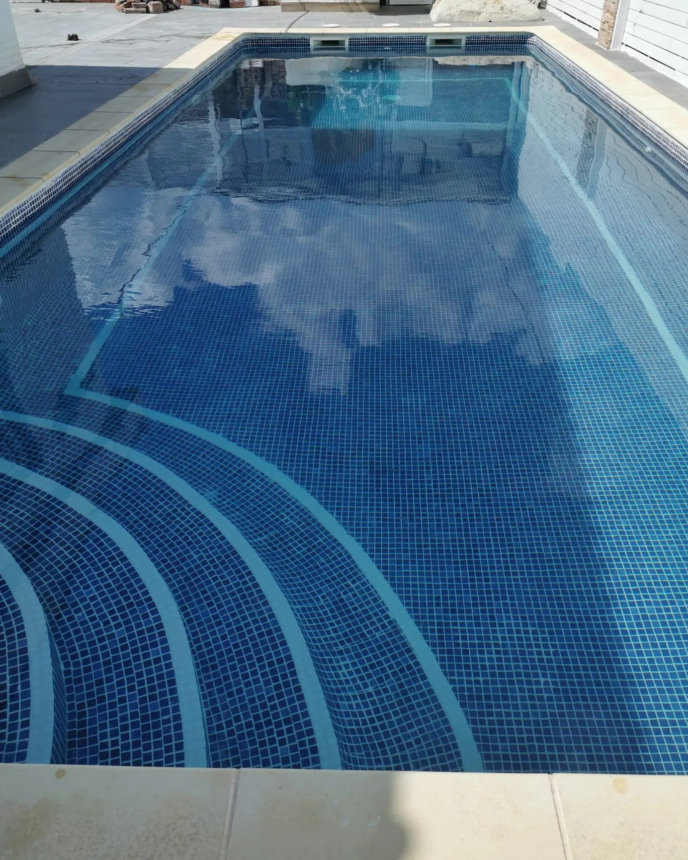 Piscina rectangular llena de agua limpia con el fondo de gresite azul y una cenefa curva en los escalones