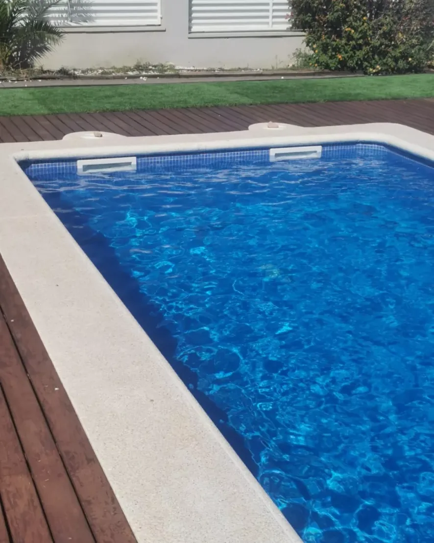 Piscina rectangular con revestimiento azul y tarima de madera en el borde