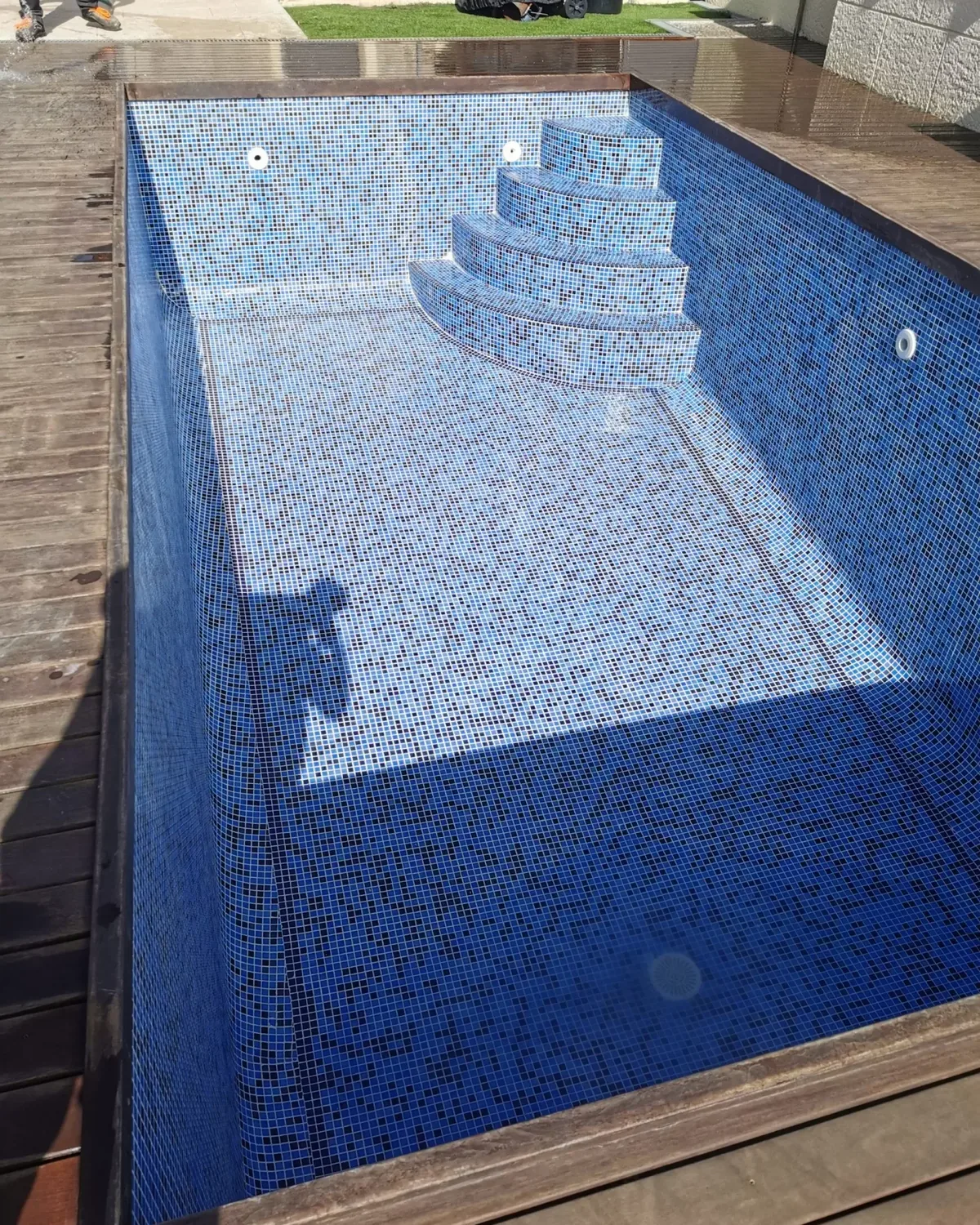 Piscina vaciada revestida de gresite azul con escalones redondeados en una esquina