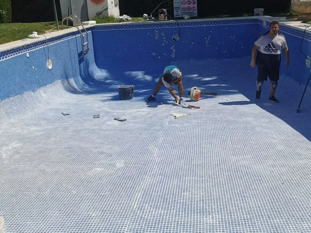Dos operarios trabajando dentro de una piscina vaciada revestida de gresite azul