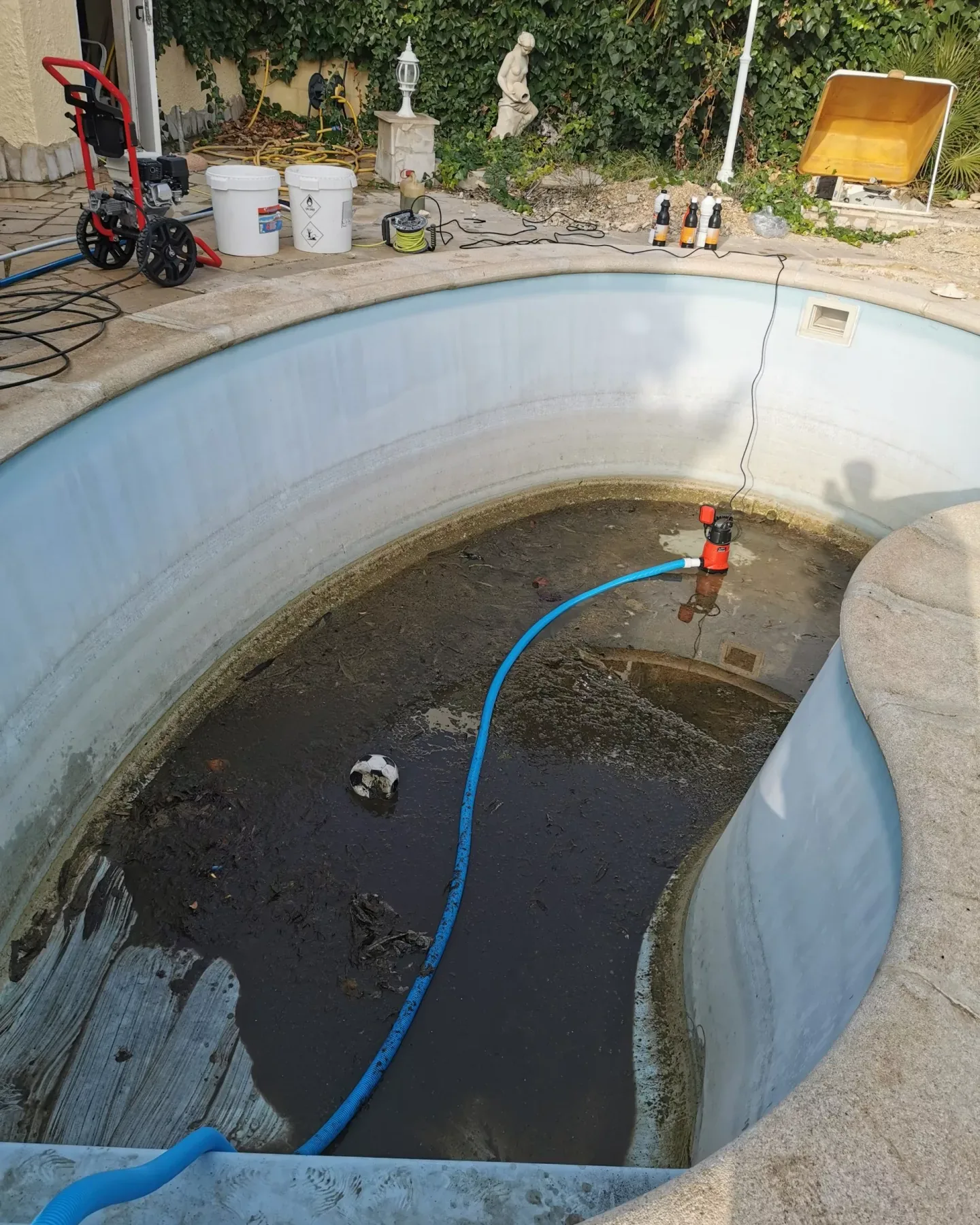 Piscina vaciada durante la limpieza, con una bomba sumergible achicando el agua sucia del fondo y los equipos en el borde